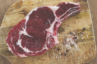 Raw rib eye steak, cowboy steak, on a wooden chopping board, top view, no people