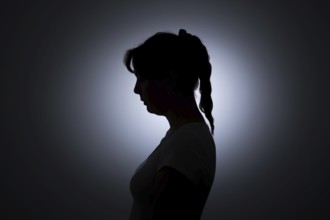 Symbolic photo on the subject of loneliness in woman. The silhouette of a young woman stands out