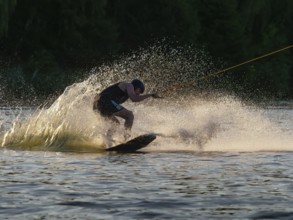 Man with wakeboard in splashing water, evening light, water sports and water skiing in wakepark