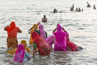 Hindu pilgrims, woman in colourful saris, take a holy dip in the sea in front of sunrise at Ghat