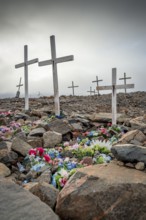 White crosses mark flower-decorated graves in a cemetery in foggy weather, remote Arctic Inuit