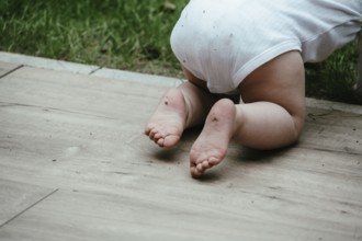 A baby crawls on a wooden floor in the garden