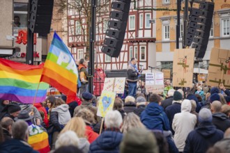 Speaker on a stage at a demonstration, group of people with a large peace flag and banners, Against