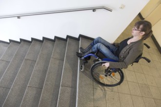 Young woman in a wheelchair stands with her wheelchair in a stairwell of a building in search of