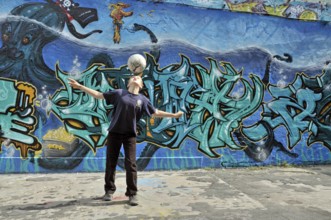 A ten-year-old boy plays with his football in front of a graffiti wall, Germany, Europe