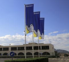 Company flags with logo Bibendum figure flying outside, Michelin factory and research