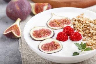 Yoghurt with raspberry, granola and figs in white plate on a gray concrete background and linen