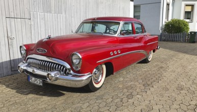 A shiny red classic car with chrome details parked in front of a white garage door, classic car,