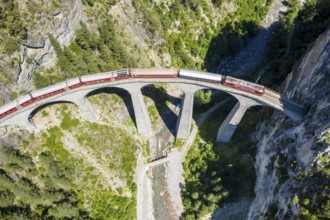 Drone shot of train passing the Landwasserviadukt near Filisur, red train of Bernina Express,