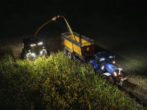 Two tractors harvesting a maize field at night and loading it, Maize harvest, Dachtel, Black