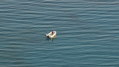 Single boat with one person on calm blue sea in the distance, Anthony Quinn Bay, Vagies Bay,