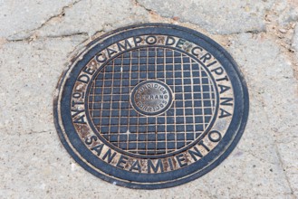 A round metal manhole cover with text engraving on a tarmac road, manhole cover, Campo de Criptana,