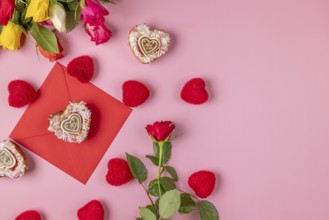 Valentine's Day composition with roses, hearts and envelope, heart-shaped cupcakes, on a pink