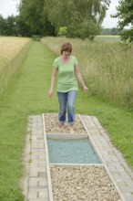 Woman walking barefoot over glass gravel and bottle corks, barefoot path Tilbeck Abbey, Havixbeck,