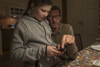 Father and daughter, 10 years old, looking for something with their mobile phone,