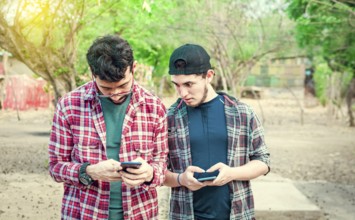 Jealous friend spying on his friend's cellphone outdoors, Friend spying on his friend phone. A guy