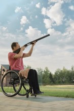 Outdoor portrait of a senior man using a wheelchair, holding a rifle up to the sky waiting for