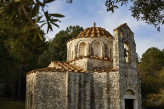 Historic church with red tiled roof and bell tower, surrounded by trees and blue sky, Byzantine