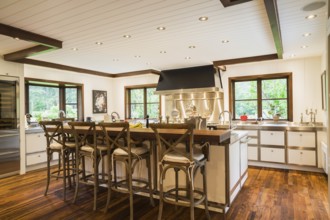 Country style kitchen with island and rustic wooden high chairs inside a New Hampton style home,