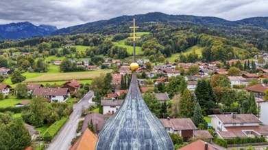 Village view with church spire cross, surrounded by green hills and wooded mountains, under a