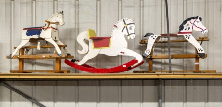 Three wooden rocking horses in a line on display in auction room, UK