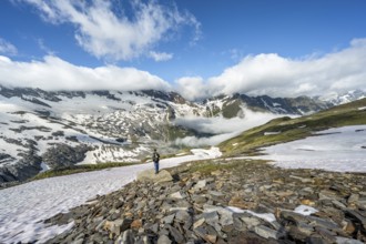 Mountaineer in front of mountain landscape with snow fields and high fog in the valley, in the