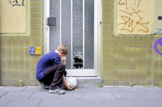 Crying ten-year-old boy Ten-year-old in front of the smashed glass pane on a front door, Germany,