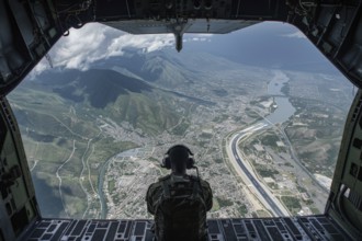 A soldier sits at the open hatch of a Hercules C-130 military cargo plane and looks at the