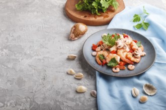 Boiled shrimps or prawns and small octopuses with herbs on a blue ceramic plate on a gray concrete