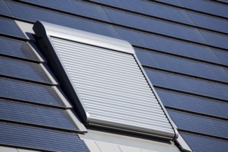 Roof window with roller shutter on a detached house with photovoltaic tiles. Photovoltaic tiles are