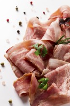 Raw bacon, sliced, with micro greenery and spices, on a white background, close-up