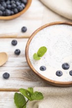 Yogurt with blueberry in wooden bowl on white wooden background and linen textile. Side view, close