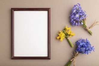 Wooden frame with spring snowdrop flowers bluebells, narcissus on beige pastel background. top