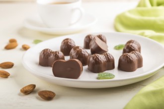 Chocolate candies with almonds and a cup of coffee on a white wooden background and green textile.