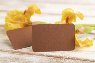 Brown business card with iris yellow flowers on white wooden background. side view, copy space,