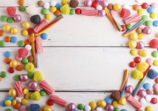 Colorful frame of multicolored candies on white wooden background. Circle copy space, top view,