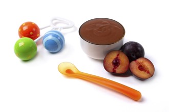 Baby food, plum puree, on a white background, with a spoon and a rattle, horizontal, no people, top