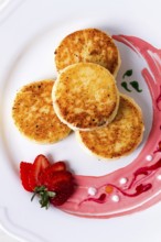 Cottage cheese pancakes, on a white plate decorated with sauce, fresh strawberry berry, close-up,