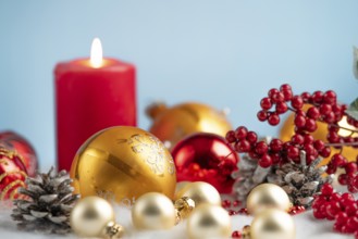 Christmas decorations with red and gold baubles, a burning candle and pine cones against a blue