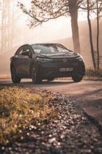 A Volkswagen stands on an autumn road in the light of the setting sun and surrounded by trees,