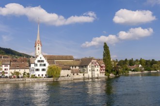 Church with high tower on the riverbank, surrounded by half-timbered houses and trees, view of the