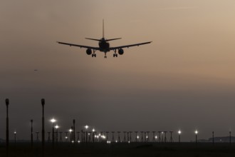 Airbus jet passenger aircraft on approach to land at sunset over landing lights, London Stansted