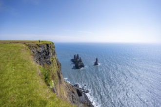 Young man standing on cliff, view from steep cliff to the rocks Reynisdrangar in the water, at