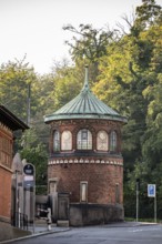 A small round brick tower with a green copper roof against a wooded background, watchtower,