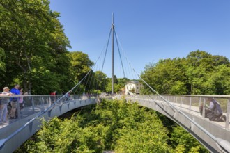 Modern bridge over dense forest, numerous walkers enjoying the sunny day, Rügen, chalk coast