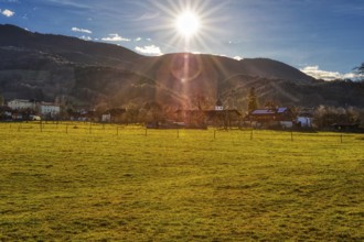 The sun sets over a village that lies in front of a mountain range and is surrounded by green