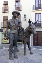 Bronze statue of a man with a donkey in front of a historic building by day, Granada