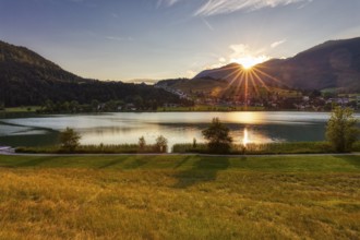 Sunset over a lake with mountains and meadows, radiant light and reflection in the water, Thiersee