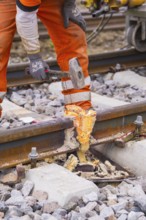 A construction worker works on a spot on the track with a hammer, surrounded by stones, Hermann