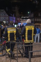 Two firemen in uniforms watching a crowd at night on a paved square, carnival, Calw, Black Forest,